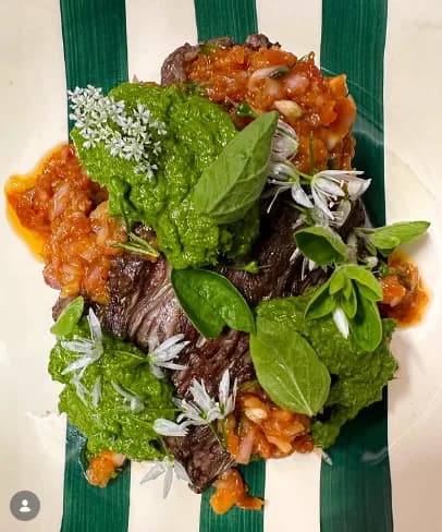 Bœuf accompagné d'un pesto d'herbes fraîches et de fleurs comestibles sur une assiette à rayures vertes