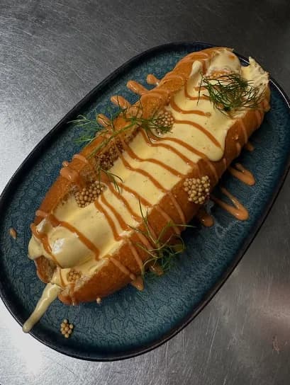 Éclair salé crémeux nappé de sauce, présenté sur une ardoise sombre