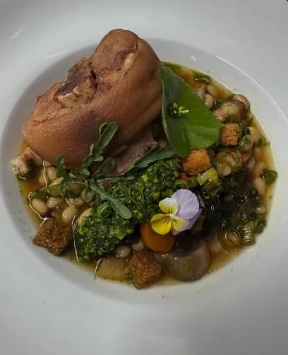 Jarret de cochon confit, cocos de Paimpol et pesto d'herbes, dressé dans une assiette blanche