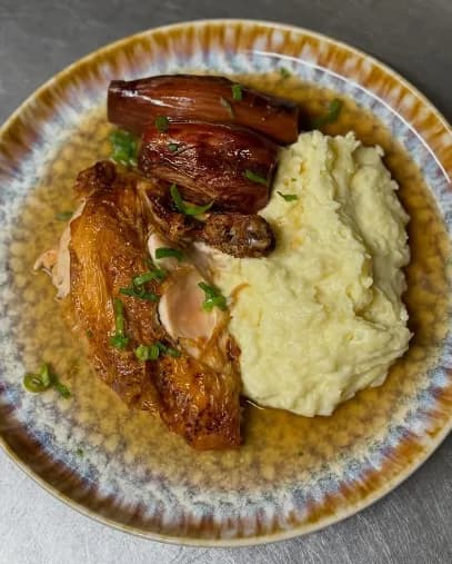 Poulet rôti maison, purée onctueuse et échalotes confites servis dans une assiette en grès