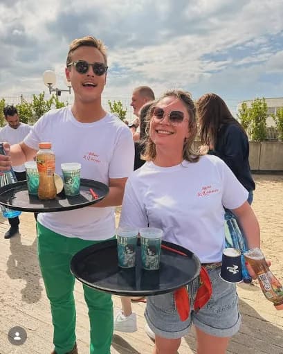 Deux serveurs du Petit Beaumont portant des plateaux de boissons lors d'un événement en extérieur ensoleillé