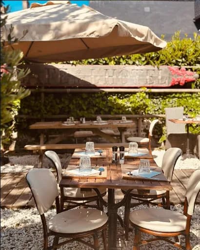 Terrasse ombragée du Petit Beaumont avec parasol, tables et chaises en bois dans un jardin ensoleillé