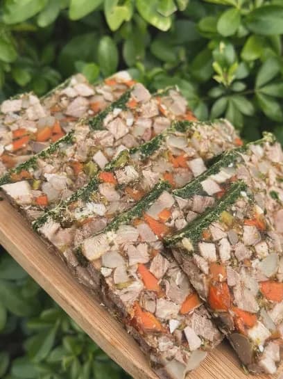 Tranches de terrine maison aux légumes et fines herbes posées sur une planche de bois, feuillage en arrière-plan